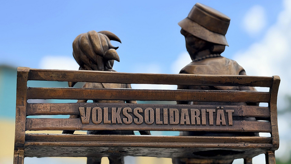 VOSO-Pine Bank von hinten Pine und Ilse Bähnert sitzen gemeinsam auf einer Bank auf der "Volkssolidarität" steht