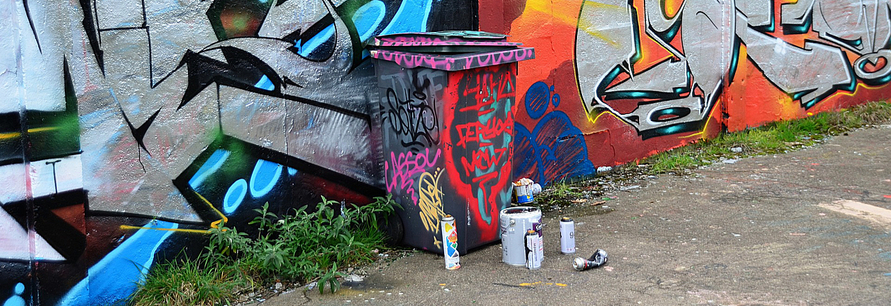 illegale Müllablagerung vor einer mit Graffiti besprühten Wand und Mülltonne