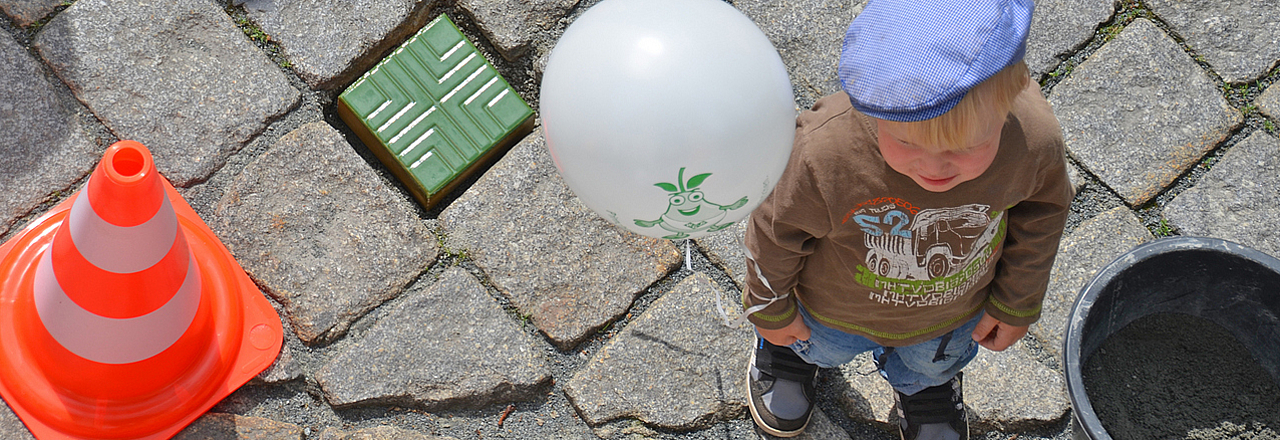 Kind steht mit Luftballon neben einem bunten Stein 