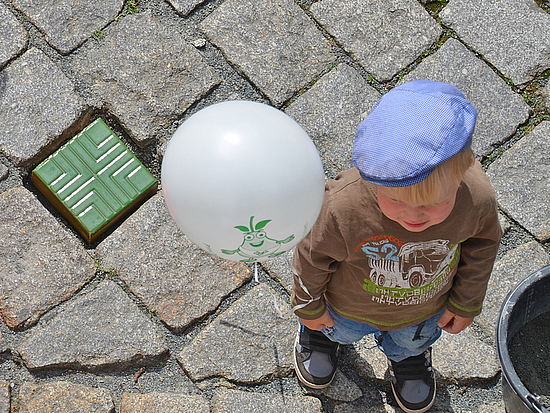 Kind steht mit Luftballon neben einem bunten Stein 