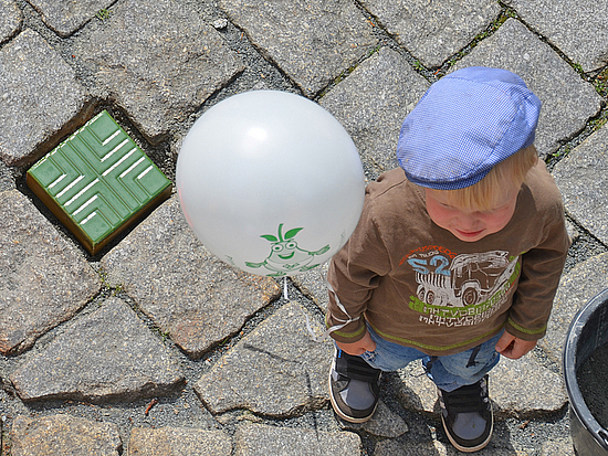 Kind steht mit Luftballon neben einem bunten Stein 
