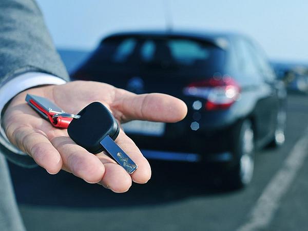 Autoschlüssel auf einer Hand vor einem Auto als Symbol für Carsharing