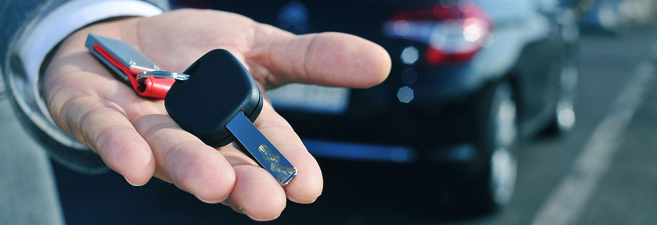 Autoschlüssel auf einer Hand vor einem Auto als Symbol für Carsharing
