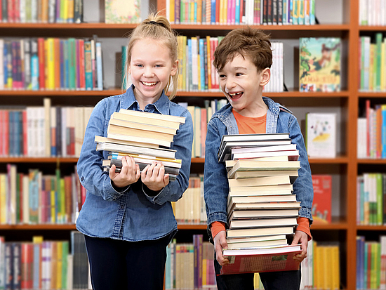 Kinder mit einem Bücherstapel in einer Bibliothek