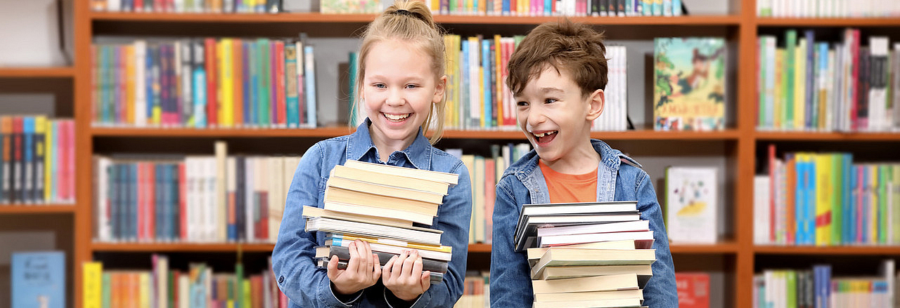 Kinder mit einem Bücherstapel in einer Bibliothek