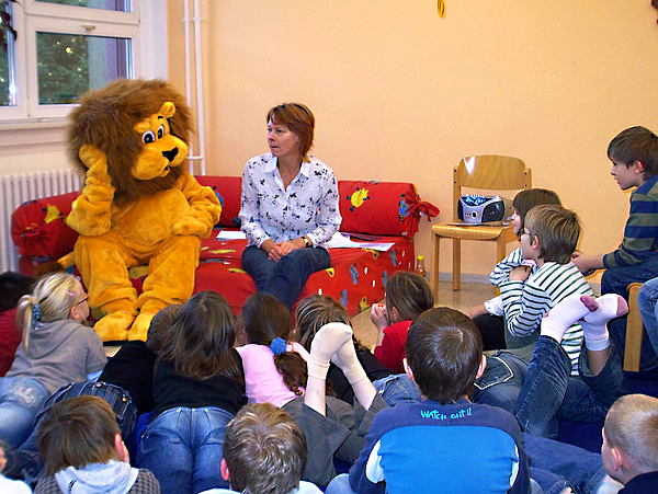 Vorlesepatin und Maskottchen Bibolin lesen Kindern in der Bibliothek vor