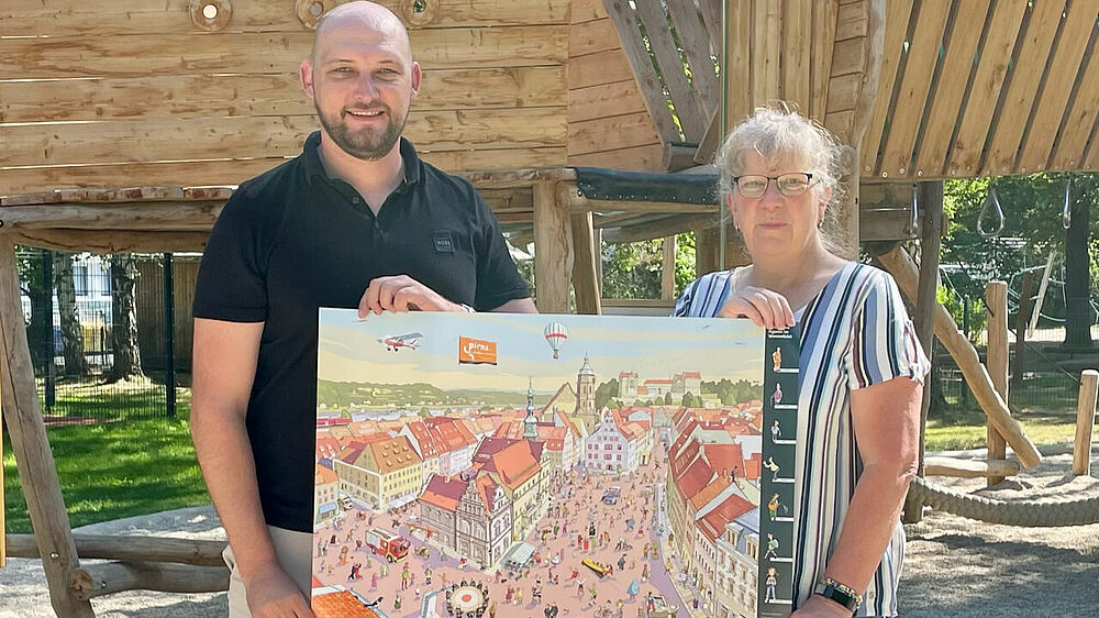 Robert Körner übergibt ein Wimmelbild-Poster an die Leiterin der Kita Schlumpfenland