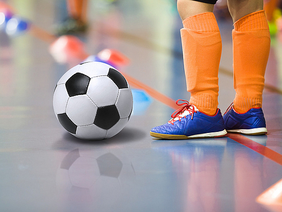 Kind spielt Fußball in einer Halle